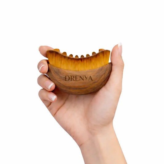 Cepillo facial de masaje de madera sostenido en la mano sobre fondo blanco.